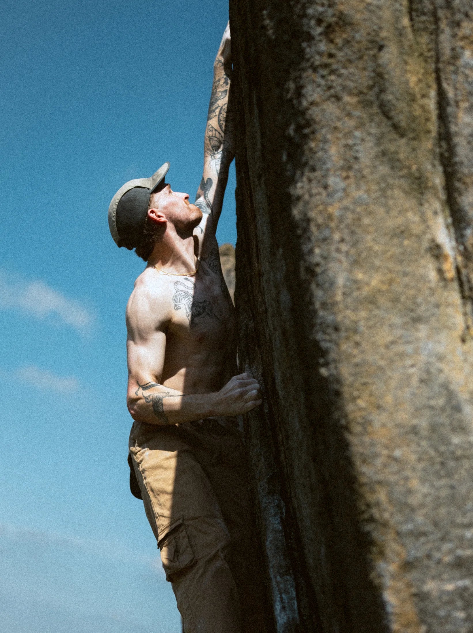 A climber at full extension on a steep gritstone edge against a blue sky.