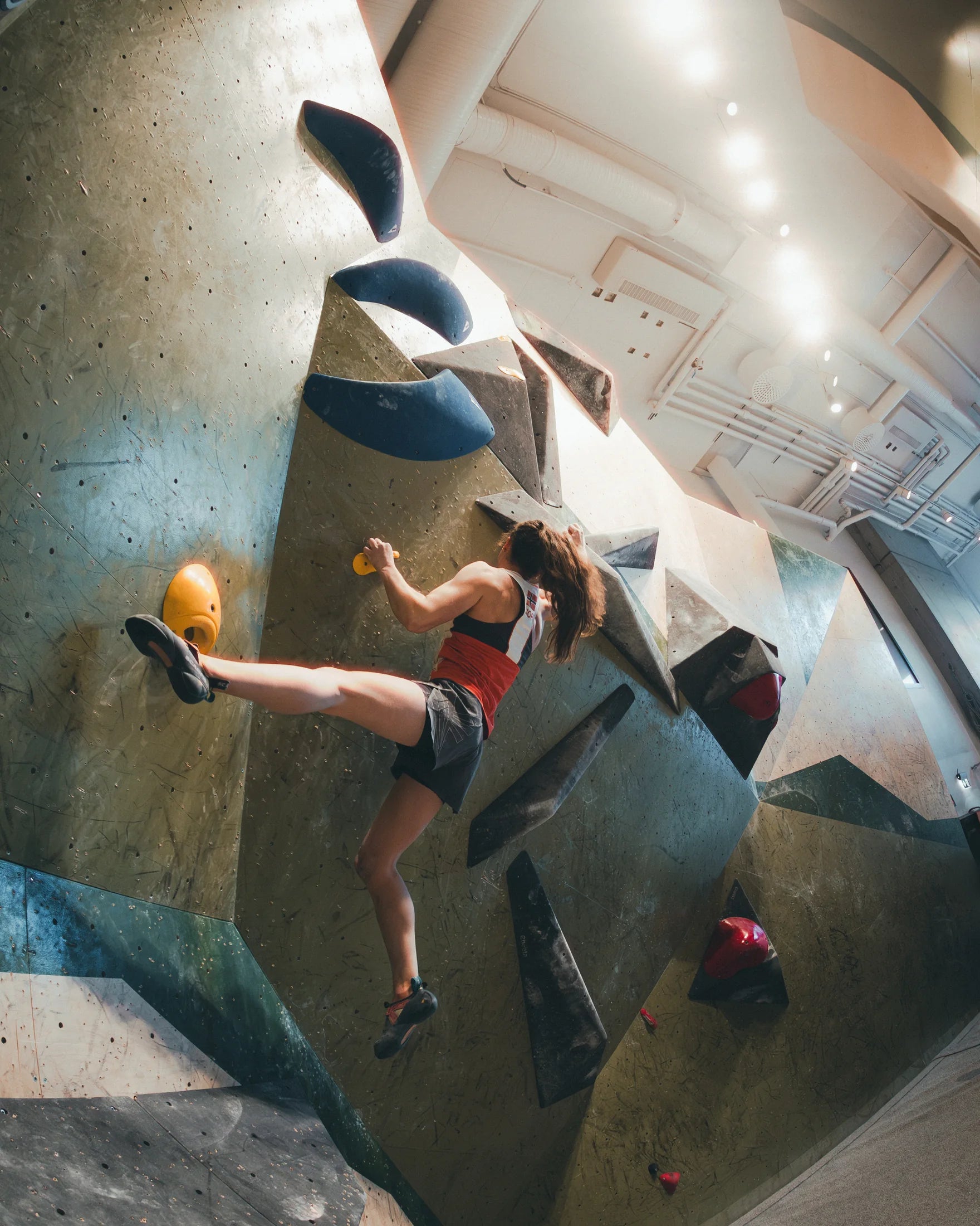 A Norwegian national-team climber moves across a competition bouldering wall in the team kit at Gneiss.