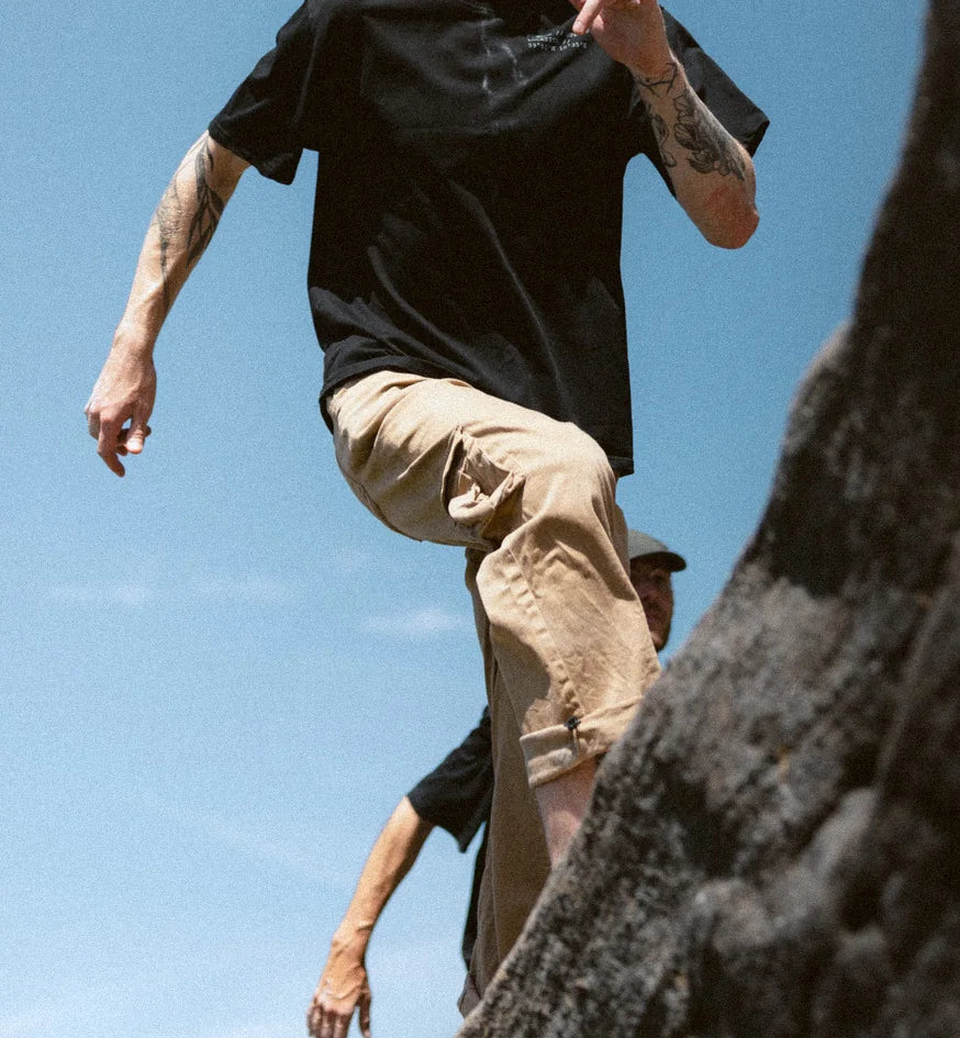 A climber steps off the top of a gritstone boulder in mid-air against open sky.